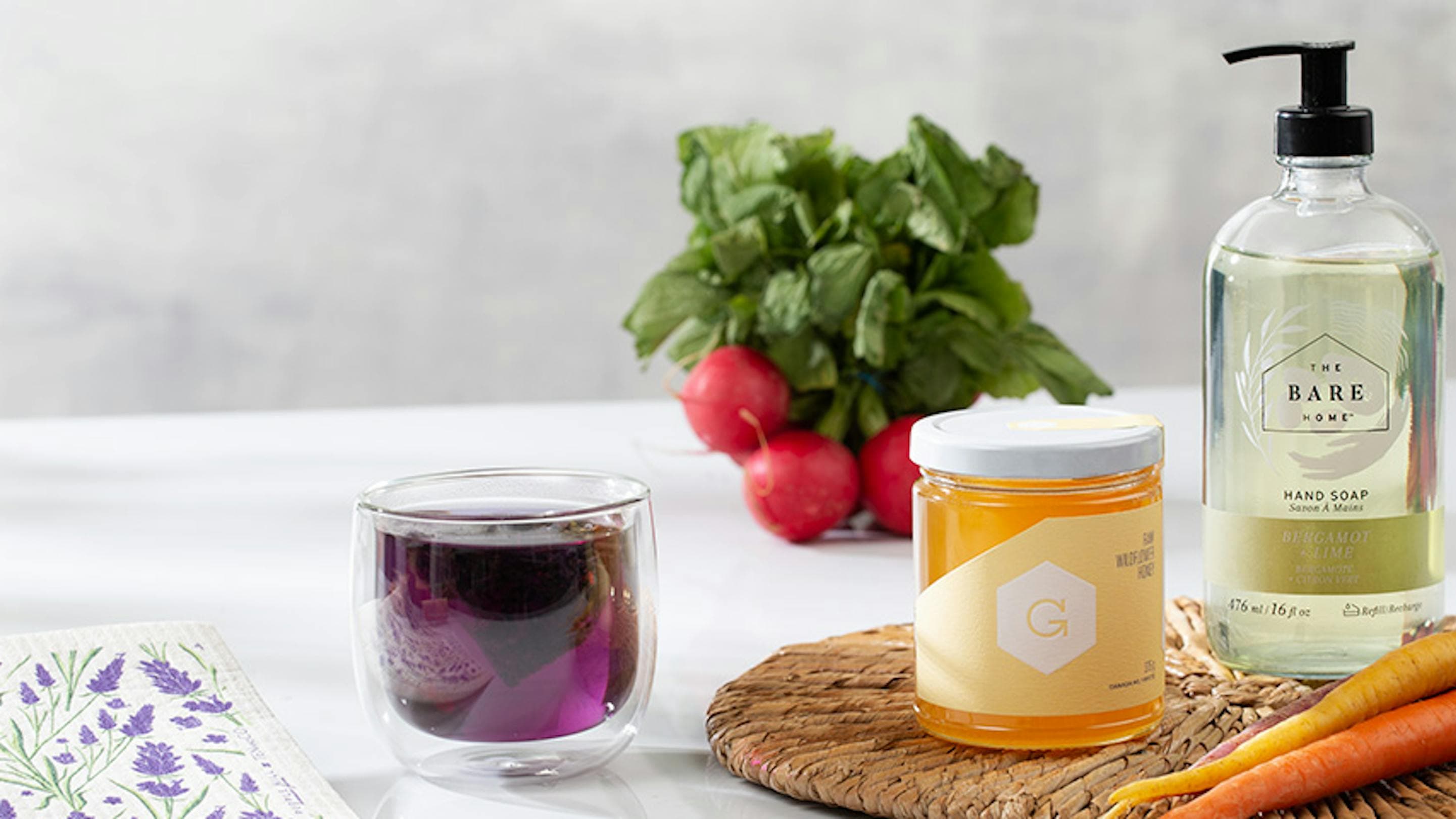 housewarming gift with honey, liquid soap, purple tea, a dishcloth and radishes in the background