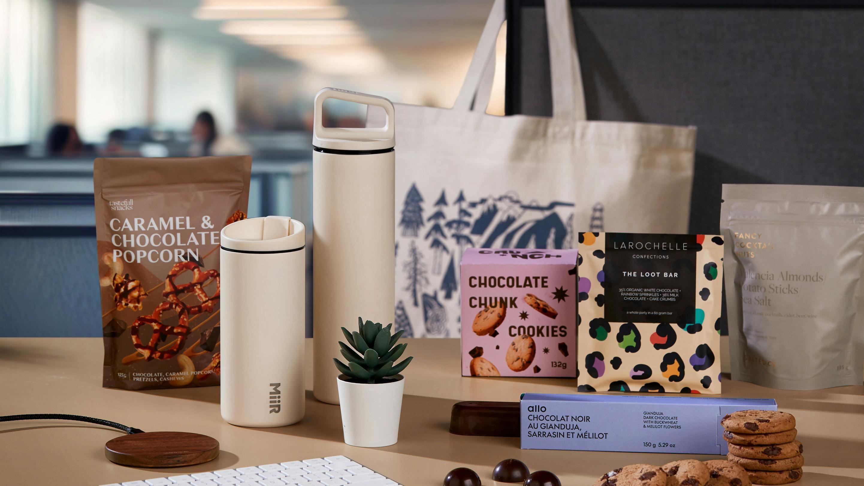 A cubicle desk with assorted artisan treats, a plant, travel mugs and a canvas bag.